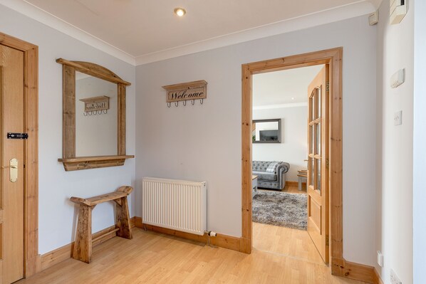 A hallway with wooden doors, a mirror, a 'Welcome' sign, and a radiator.