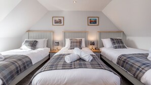 A hotel room with three single beds, each with a plaid blanket and pillows. There are two framed pictures on the wall above the beds.