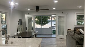 A modern kitchen with a dining area, a gray sofa, and a view of the outdoors.