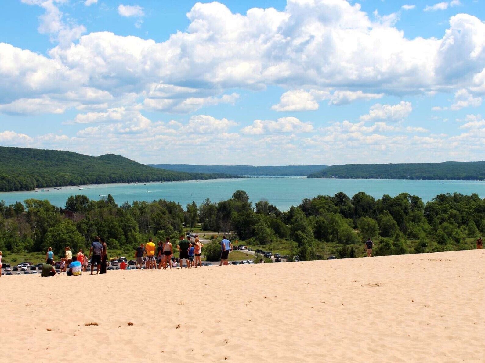A beach with a group of people, a sandy area, and a view of a large body of water with boats.