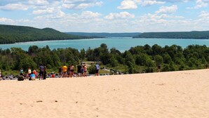 A beach with a group of people, a sandy area, and a view of a large body of water with boats.