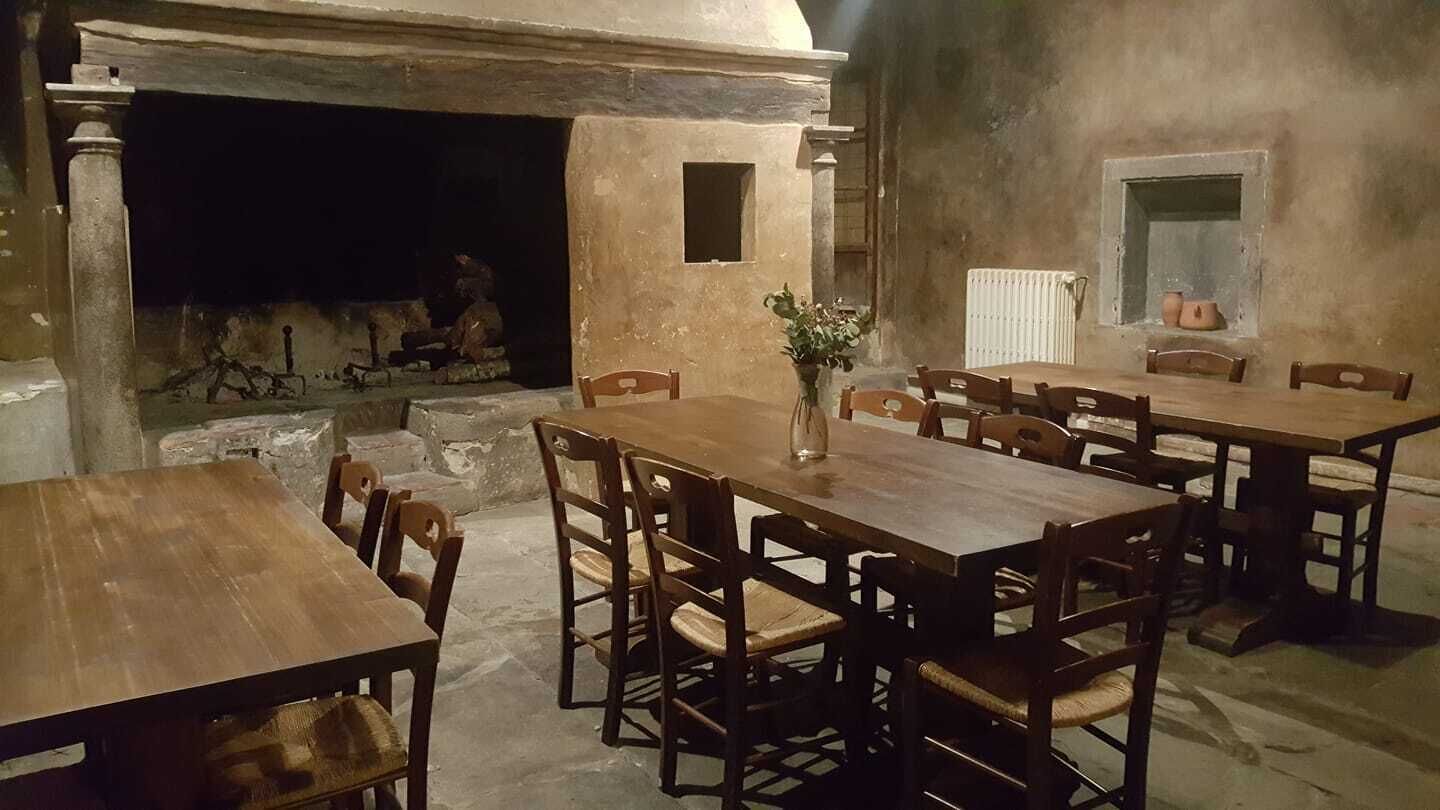 Un comedor rústico con mesas y sillas de madera, chimenea y paredes de piedra.