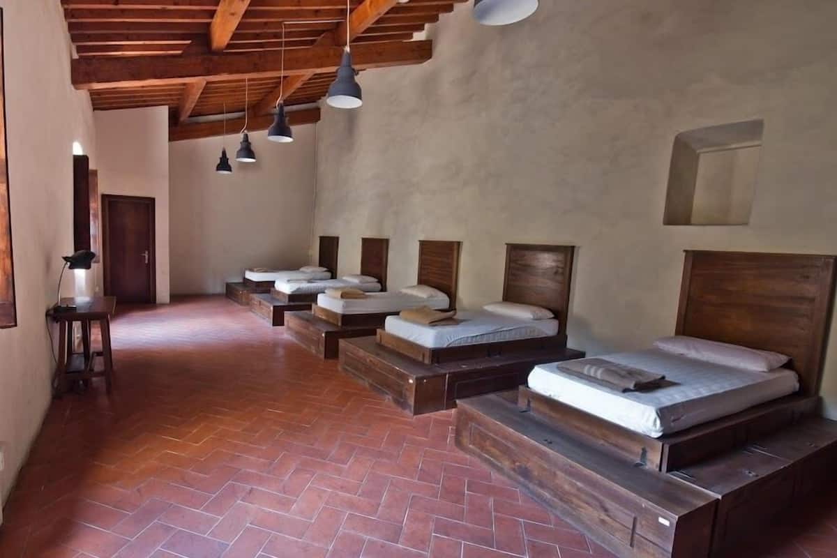 A room with multiple beds arranged in a row, wooden headboards, and a herringbone-patterned floor.