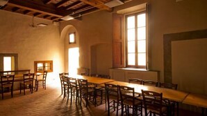 A dining room with a long wooden table and chairs, a large window with natural light, and a rustic ceiling with exposed beams. - Ostello del Bigallo - Bigallo Hostel (Bagno a Ripoli)