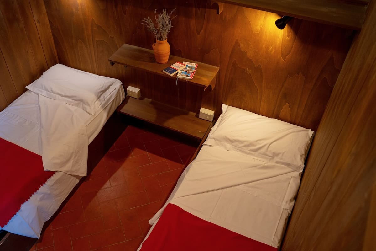 A small, cozy room with two beds, a wooden wall, a small table with a vase, and a magazine.