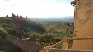 A view from a balcony with a stone wall and a wooden railing, overlooking a valley with trees and distant buildings. - Ostello del Bigallo - Bigallo Hostel (Bagno a Ripoli)