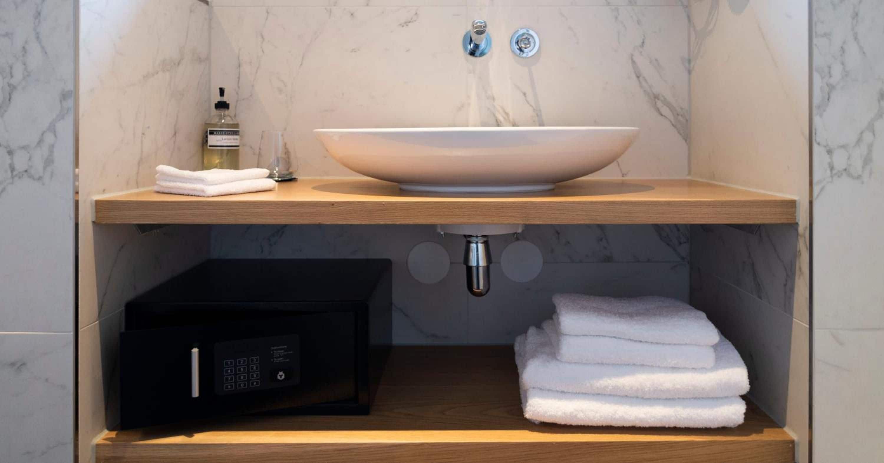 Een badkamer met een marmeren wastafel, een fles handzeep, een handdoekdispenser en een zwart elektronisch apparaat.