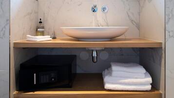 Een badkamer met een marmeren wastafel, een fles handzeep, een handdoekdispenser en een zwart elektronisch apparaat.