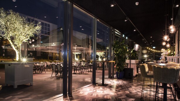 An indoor dining area with glass walls, wooden flooring, and modern lighting fixtures.