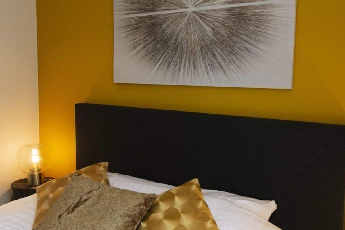 A bed with a black headboard, two pillows, and a wall-mounted abstract artwork.