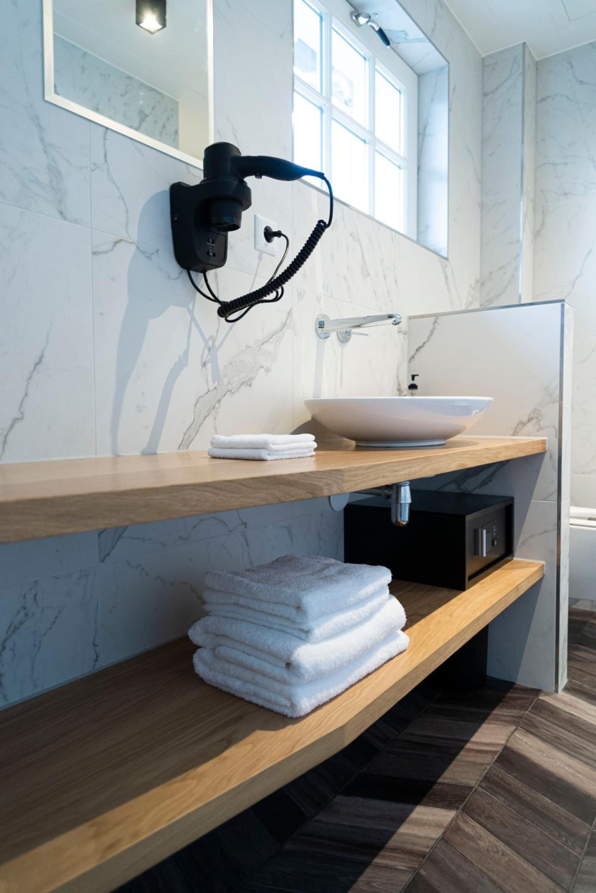 Une salle de bain moderne avec un mur en marbre, un meuble-lavabo en bois, un lavabo blanc et un porte-serviettes.