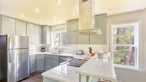 A modern kitchen with a stainless steel refrigerator, a built-in oven, a large island with stools, and a window with a view of trees. - Dog-Friendly, *HOT TUB*, Walk to Beach (Sisu) (Ocean Park)