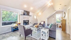 A spacious living area with a fireplace, large windows, and a loft bedroom with a view. - Dog-Friendly, *HOT TUB*, Walk to Beach (Sisu) (Ocean Park)