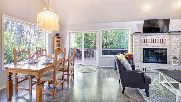 A spacious living area with a wooden dining table, comfortable seating, a fireplace, and large windows offering a view of the outdoors. - Dog-Friendly, *HOT TUB*, Walk to Beach (Sisu) (Ocean Park)