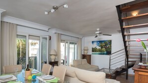 A modern living room with a glass dining table, comfortable seating, a staircase, and a view of the outdoors. - Lovely apartment for 7 guests with pool, WIFI, A/C, TV and terrace (Torremolinos)