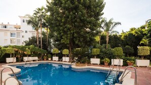 A swimming pool with steps leading into it, surrounded by greenery and white buildings. - Lovely apartment for 7 guests with pool, WIFI, A/C, TV and terrace (Torremolinos)