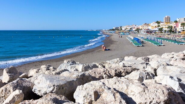 A beach with rocky foreground, clear blue sea, and buildings in the background. - Lovely apartment for 7 guests with pool, WIFI, A/C, TV and terrace (Torremolinos)