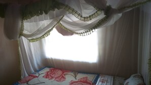 Un llit amb roba de llit floral, una finestra amb cortines translúcides i un estri amb videt blau.