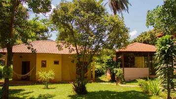 Um edifício amarelo com telhado de azulejos, rodeado por vegetação exuberante e árvores.