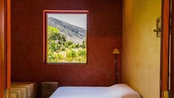 Quarto com cama, janela com vista para as montanhas, luminária de cabeceira e mesa de cabeceira pequena.