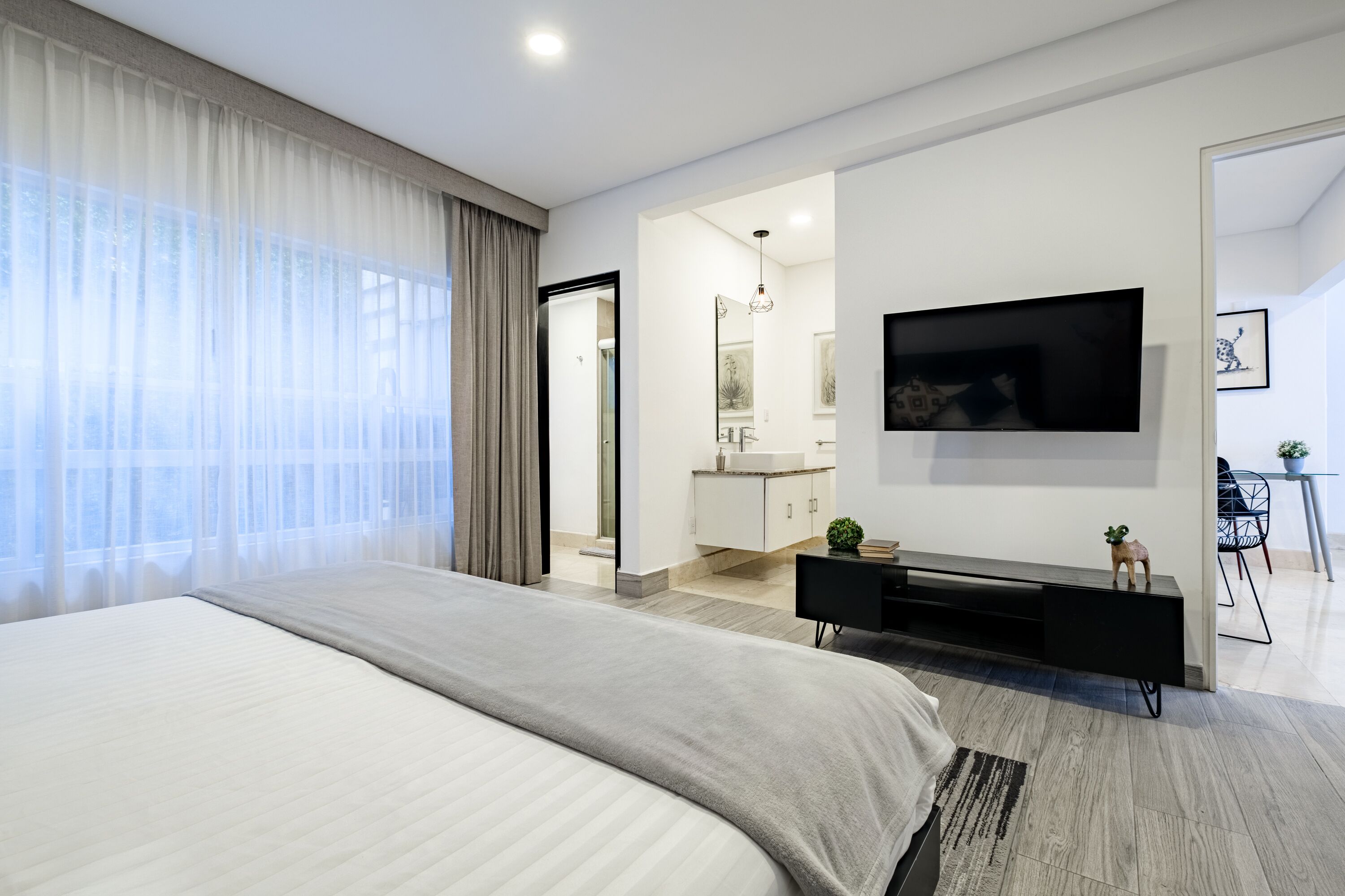 Une chambre d’hôtel moderne dotée d’un grand lit, d’un téléviseur à écran plat fixé au mur, d’un petit bureau et offrant une vue sur la salle de bain.