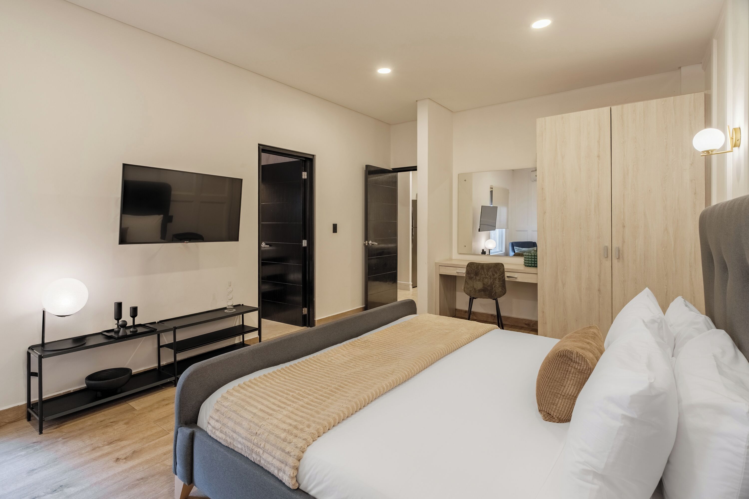A modern hotel room with a bed, a desk, a television, and a wardrobe.