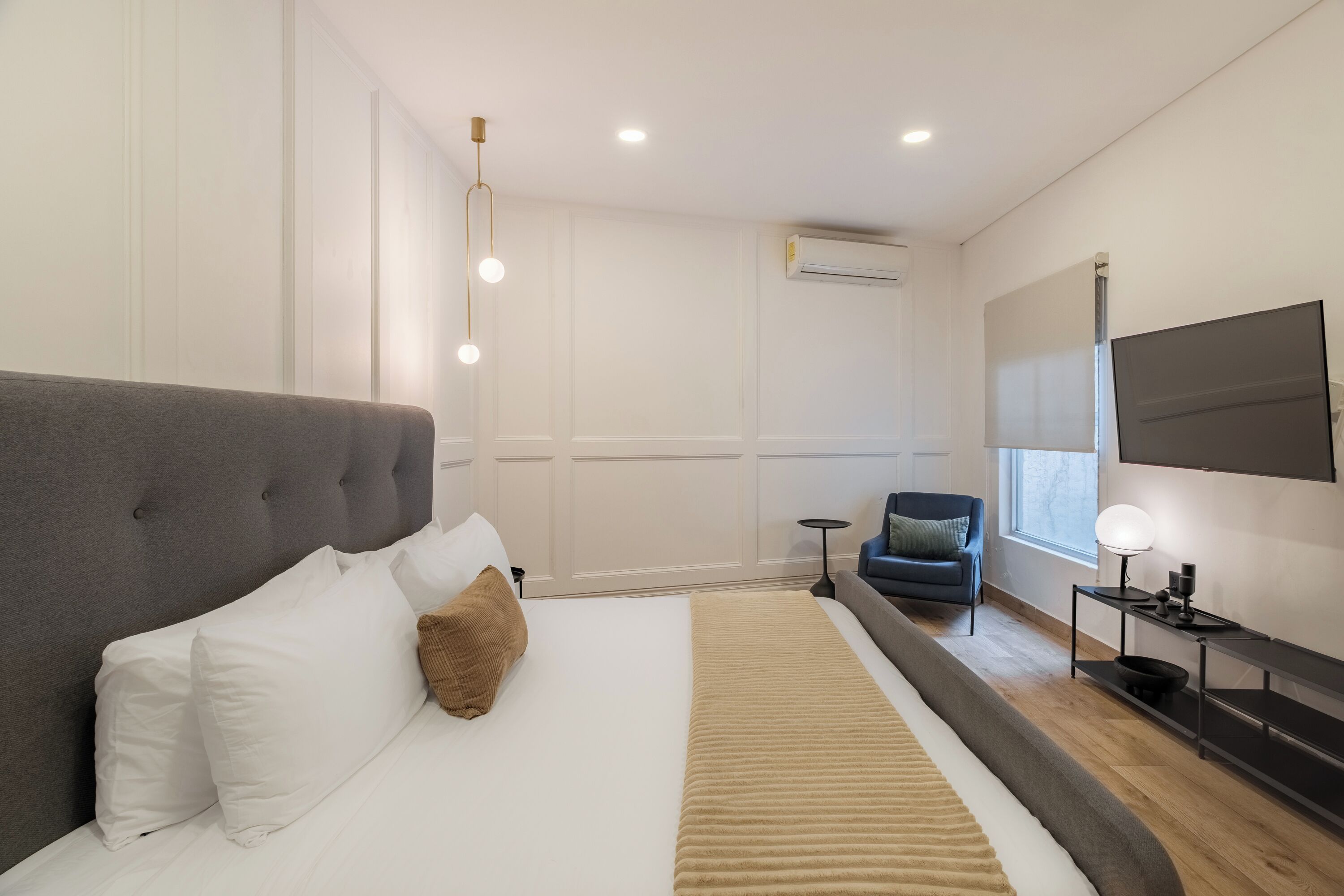 Una habitación de hotel moderna con una cama grande, un televisor montado en la pared y una mesita con una lámpara.