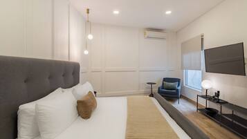 Una habitación de hotel moderna con una cama grande, un televisor montado en la pared y una mesita con una lámpara.