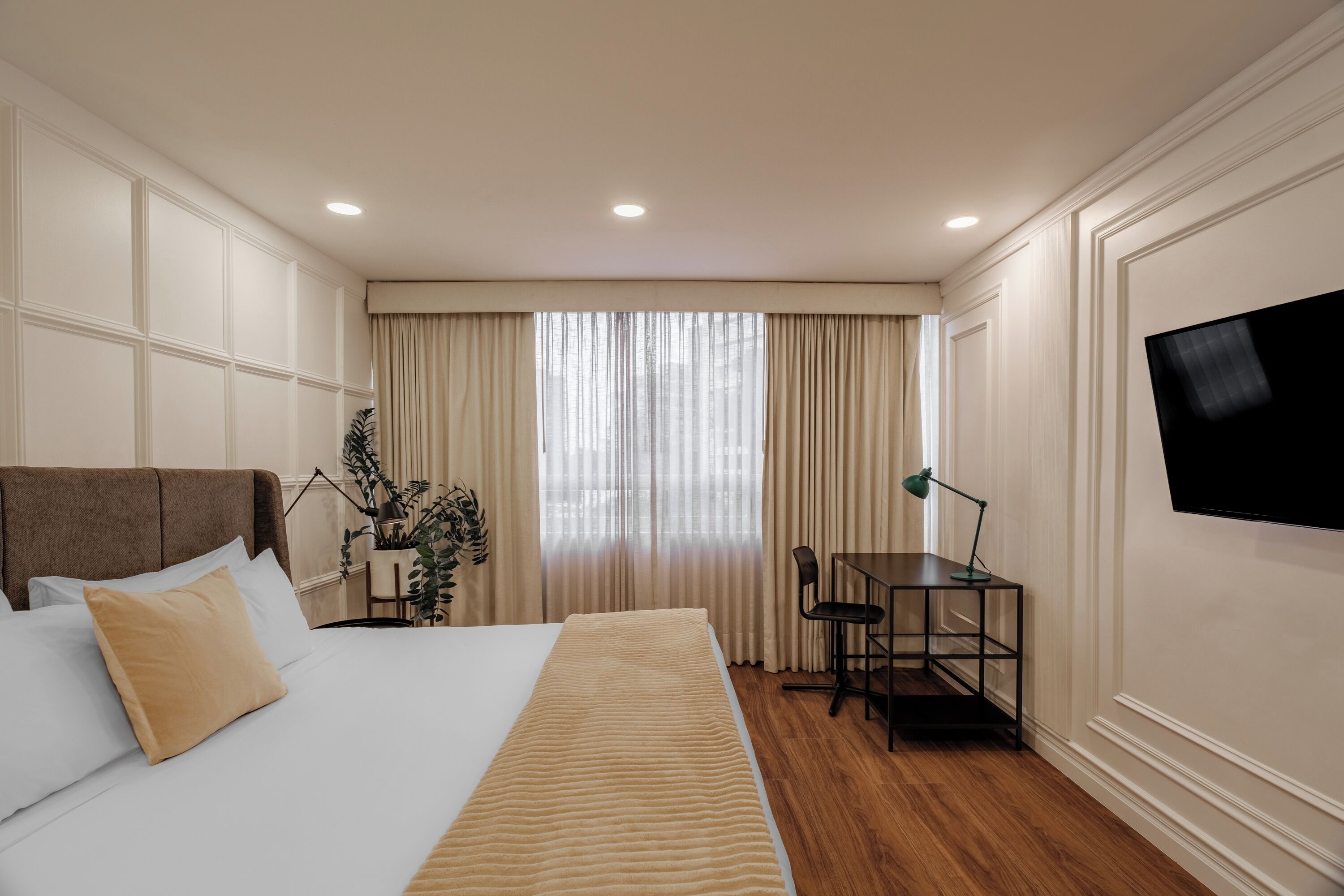 A hotel room with a bed, a desk, a chair, a television, and a window with curtains.