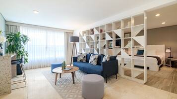 A modern living room with a sofa, coffee table, and ottoman. There is a bookshelf and a lamp.