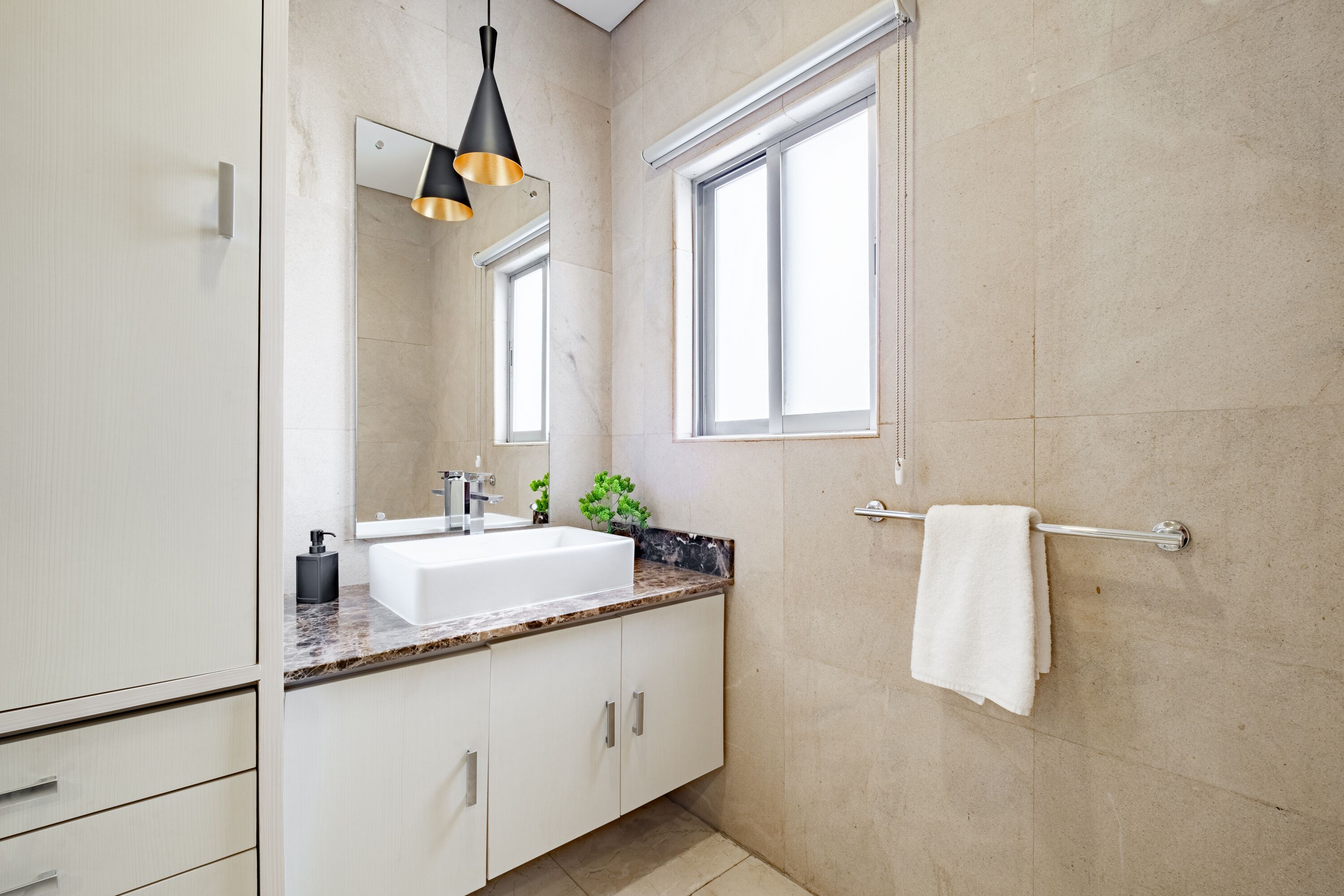 Ein modernes Badezimmer mit einem weißen Waschbecken, einem Spiegel, einem Handtuchhalter und einem Fenster.
