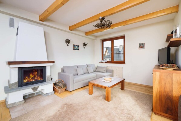 Una sala de estar con chimenea, un sofá gris, una mesa de centro de madera y un televisor sobre un mueble de madera.