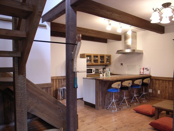 Une cuisine avec des poutres apparentes, un îlot central doté de tabourets de bar et un escalier.