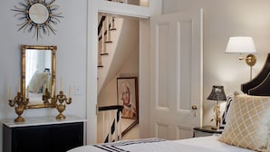 A bedroom with a bed, a nightstand, a lamp, a mirror, and a decorative wall piece.