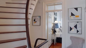 A staircase with wooden steps and a black handrail, leading to a room with a bed and a nightstand. There are abstract paintings on the walls.