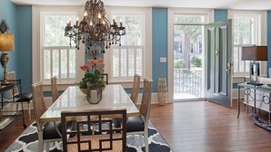 A dining room with a large table, chairs, a chandelier, and a view through the glass door.