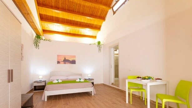 Ein Schlafzimmer mit Holzboden, einem Bett, Nachttischen, einem kleinen Tisch mit Stühlen und Blick auf die Stadt durch ein Fenster.