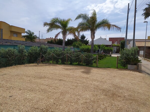 A residential area with a gravel driveway, palm trees, and a green fence.