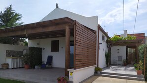 Ein Haus mit überdachter Terrasse, kleinem Garten und Holzzaun.