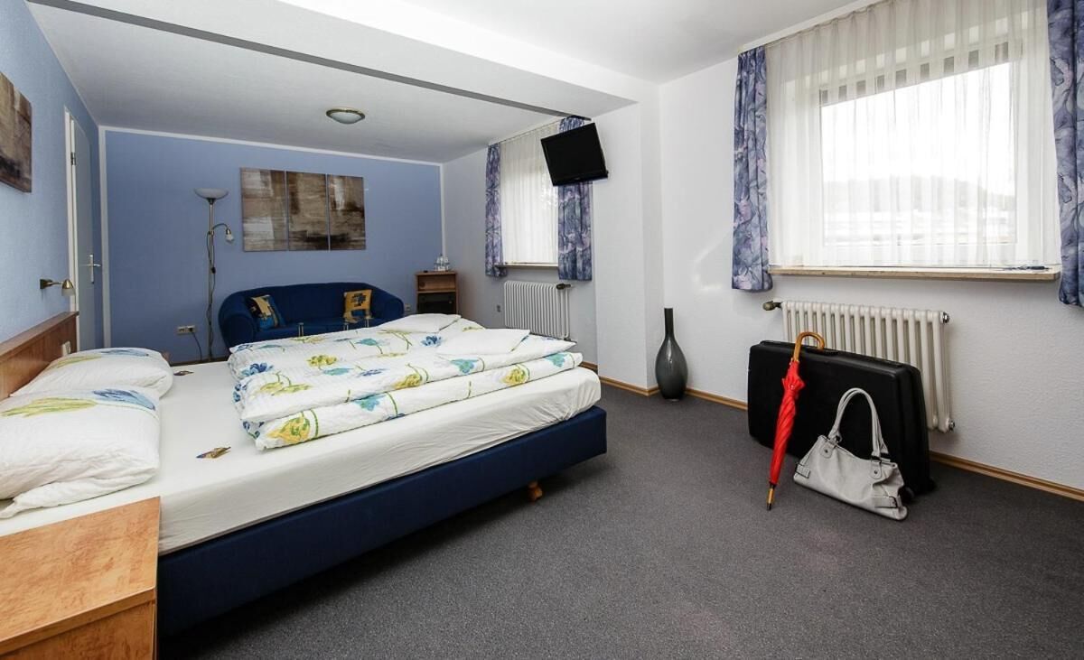 A hotel room with a bed, a desk, a chair, a radiator, a TV, and a window with curtains.