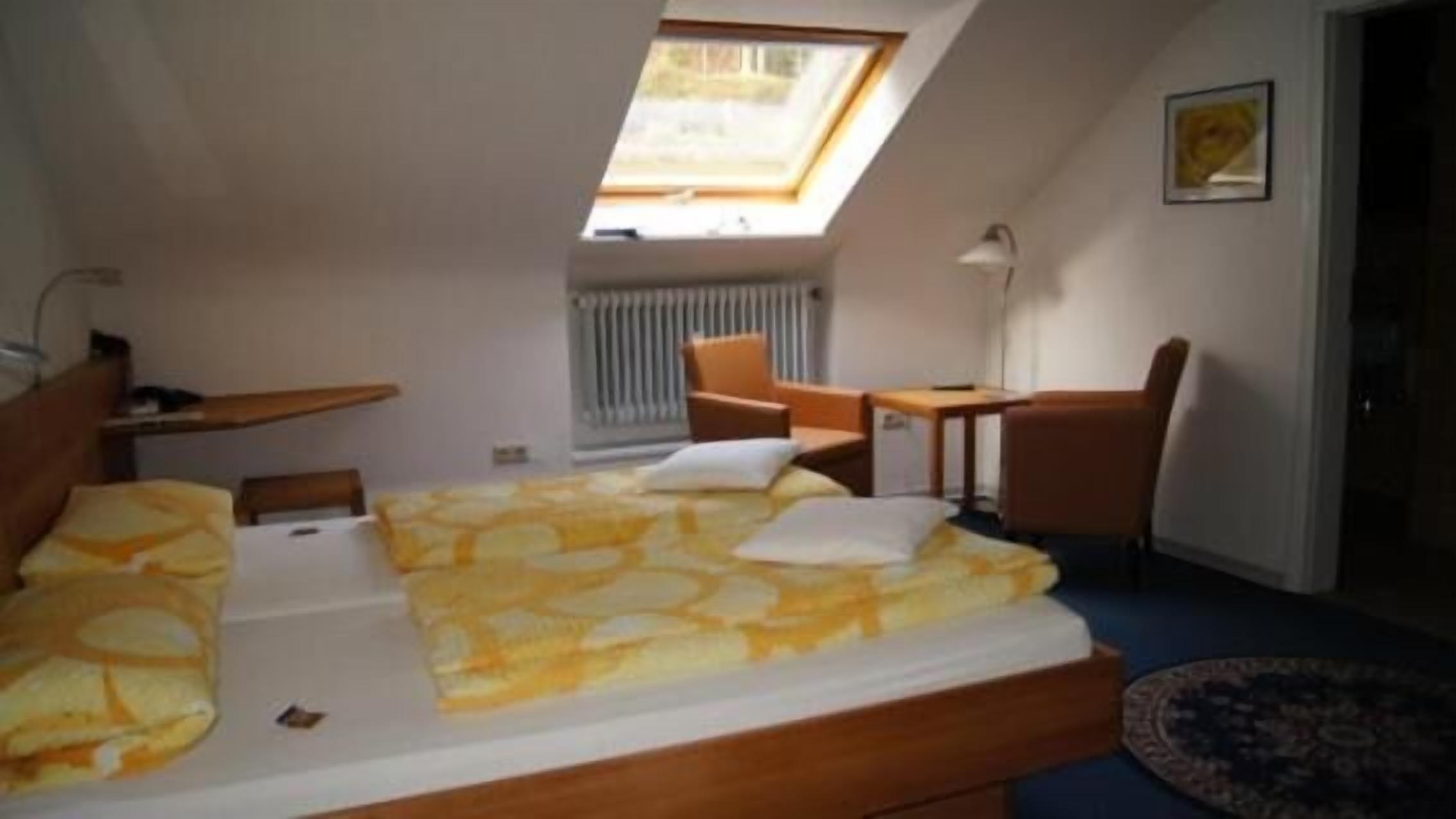 Een slaapkamer met dakraam, een bed met een beddeken met dessin, een bureau, een stoel en een radiator.