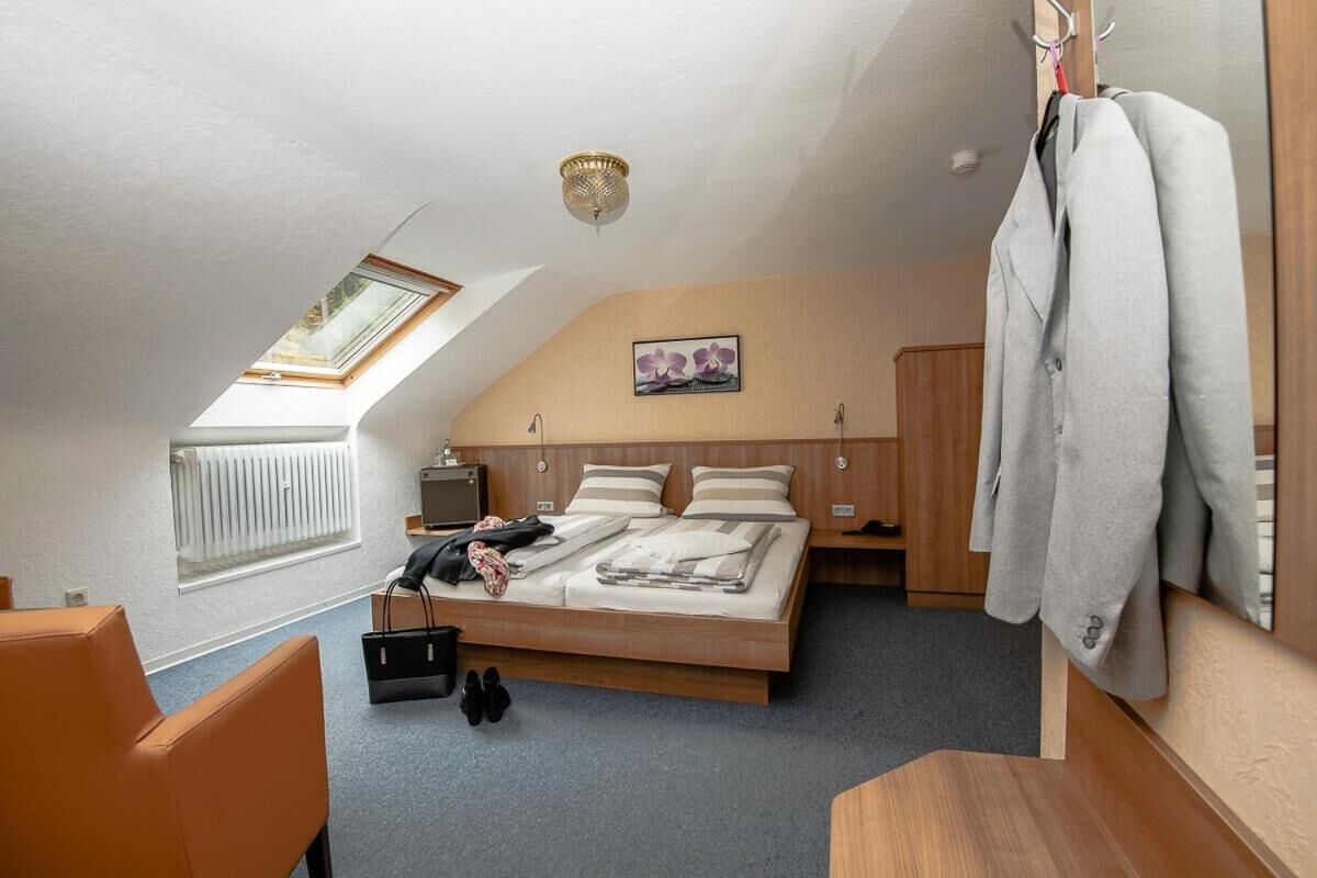 Ein Schlafzimmer mit geneigter Decke, einem Dachfenster, einem Bett mit Kopfteil, einem Nachttisch, einem Heizkörper und einem Kleiderständer mit Jacke.