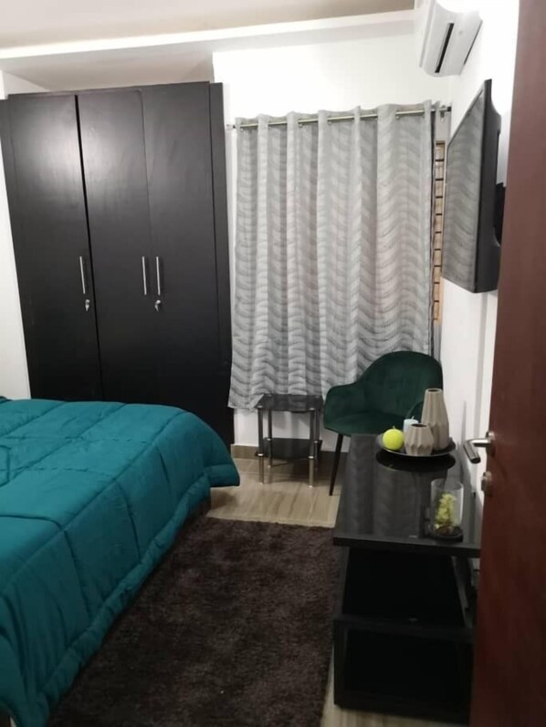 A bedroom with a bed, a desk, a chair, a wardrobe, and a curtain.