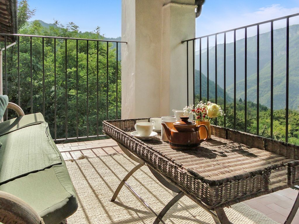 A balcony with a wicker table set for tea, a green chair, and a view of lush green mountains.