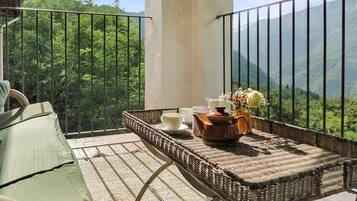 A balcony with a wicker table set for tea, a green chair, and a view of lush green mountains.