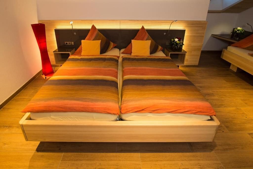 A modern bedroom with a large bed, wooden headboard, bedside tables, and a red accent piece.