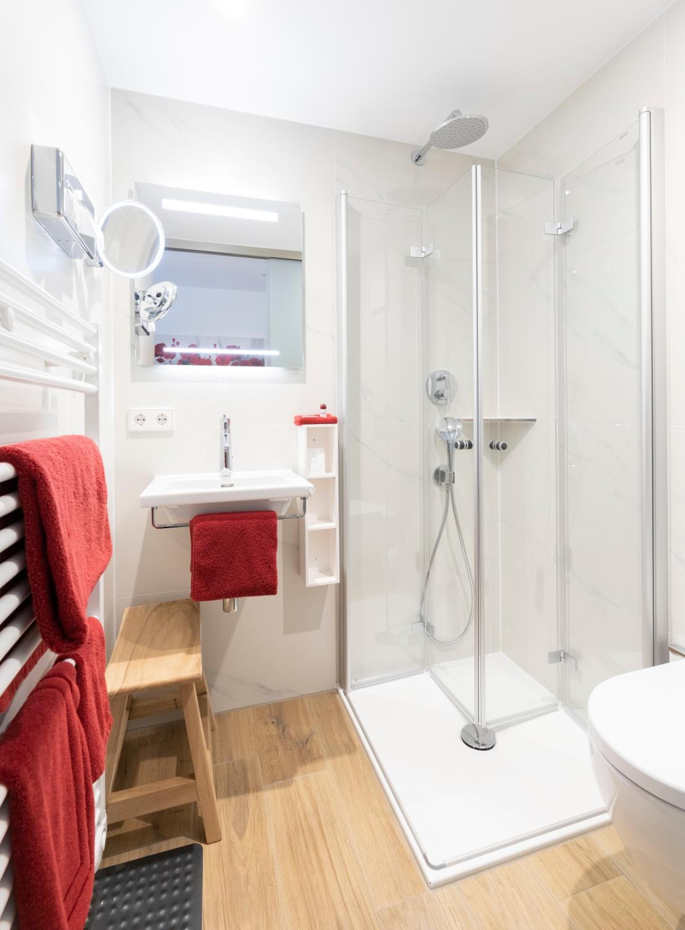 Un baño moderno con ducha acristalada, lavamanos blanco y toalla roja.