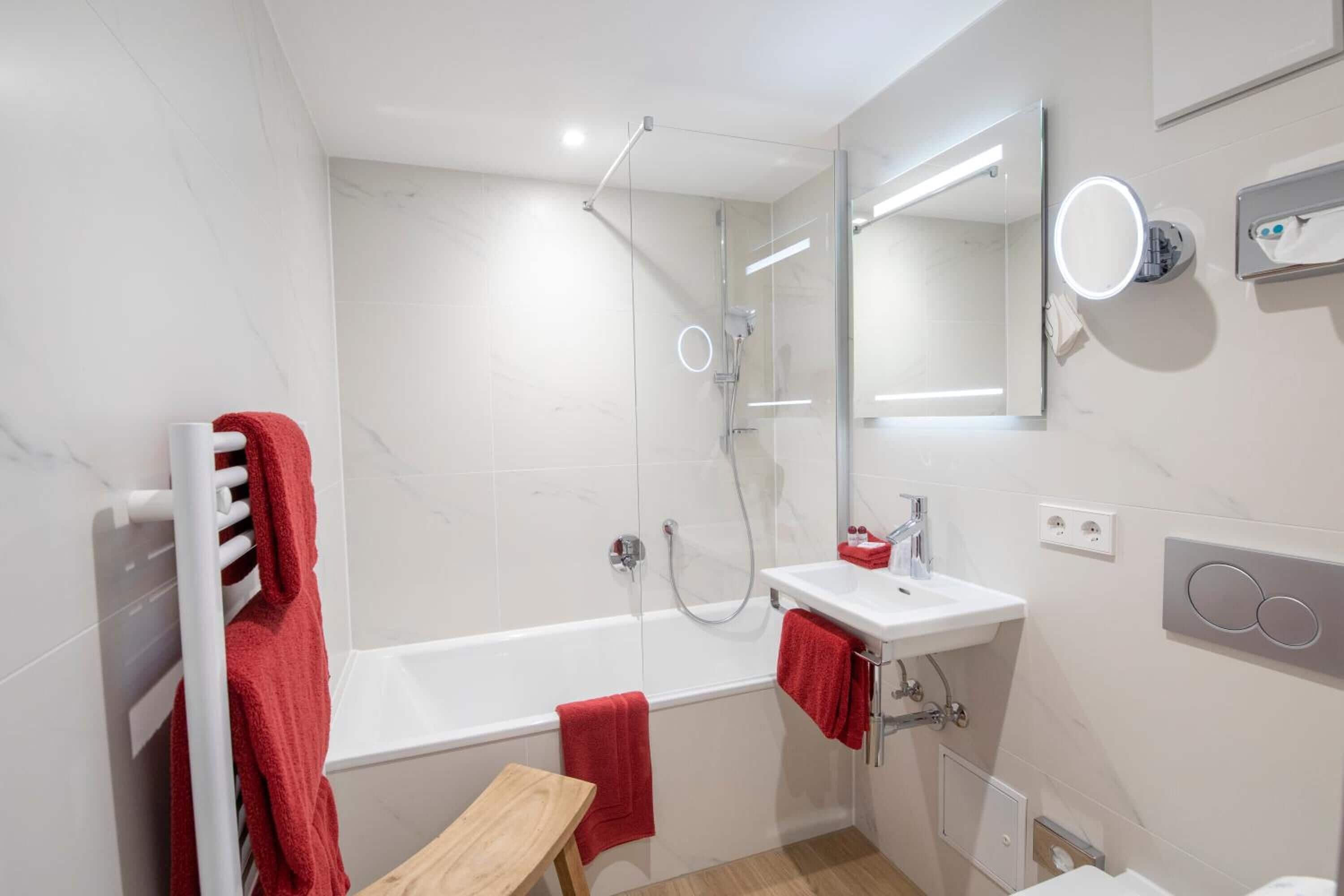 A modern bathroom with a bathtub, a shower, a sink, and a mirror with lights.