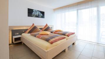 A modern bedroom with a wooden bed, a bedside table, and a large window with sheer curtains.