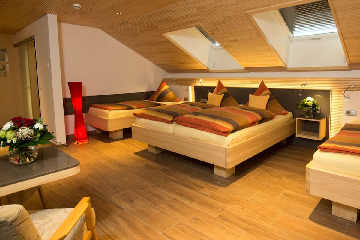 A modern bedroom with a loft-style ceiling, wooden flooring, and a central bed with multiple pillows.